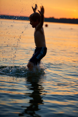 Child jumping into water at sunset