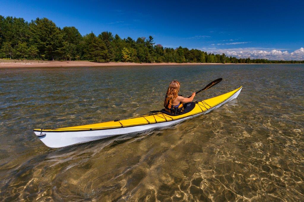 Par une belle journée ensoleillée, une femme se promène en kayak jaune sur une eau claire près du rivage. 
