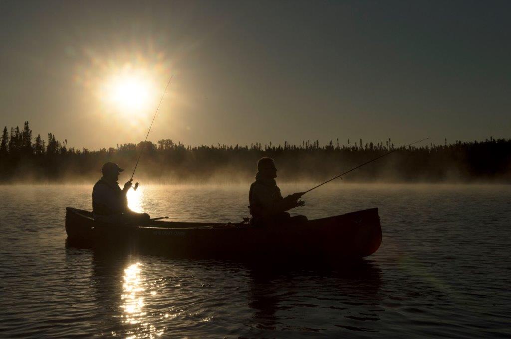 Sillouette of two paddlers fishing with a sun low in the sky