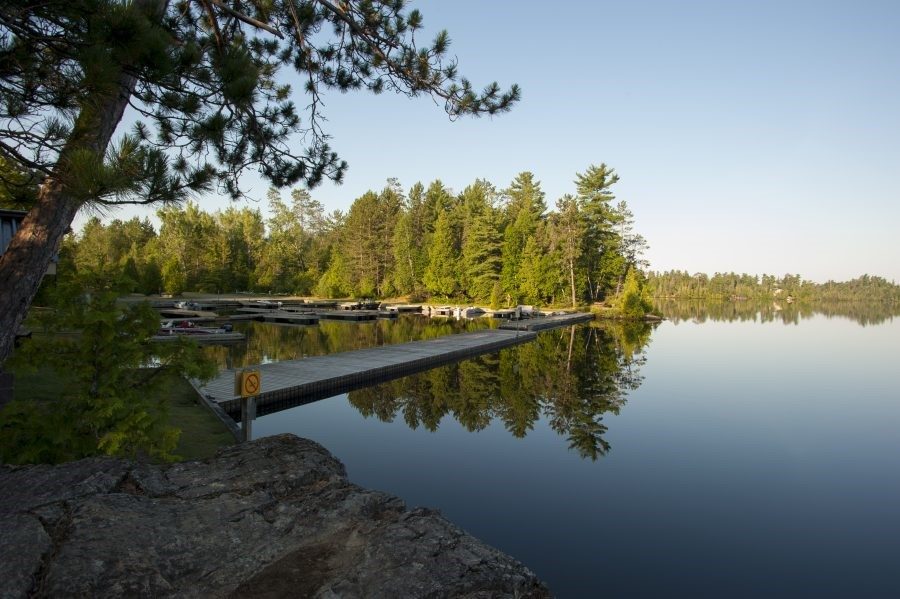 A clear lake with series of docks, with forest in the background on a blue sky day