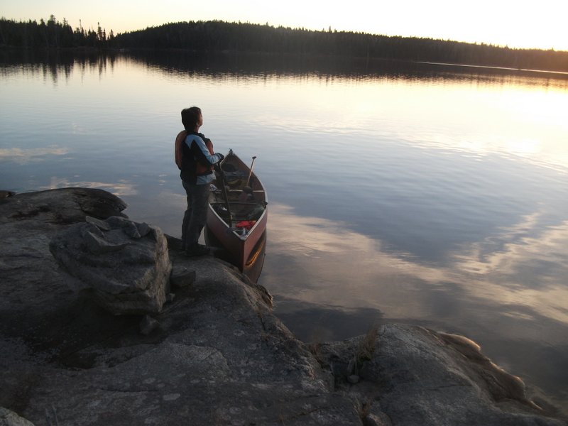 Une personne debout à côté de son canot sur le bord d’un lac 