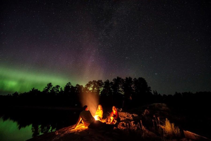 People gathered around a campfire at dark with northern lights in the background