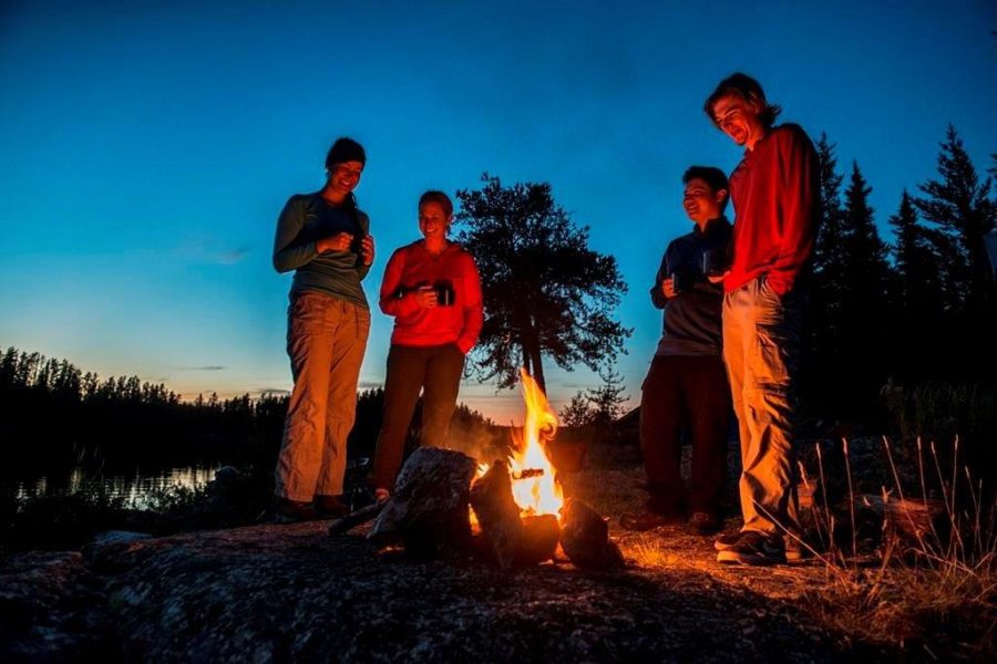 Four friends standing around a fire at dusk