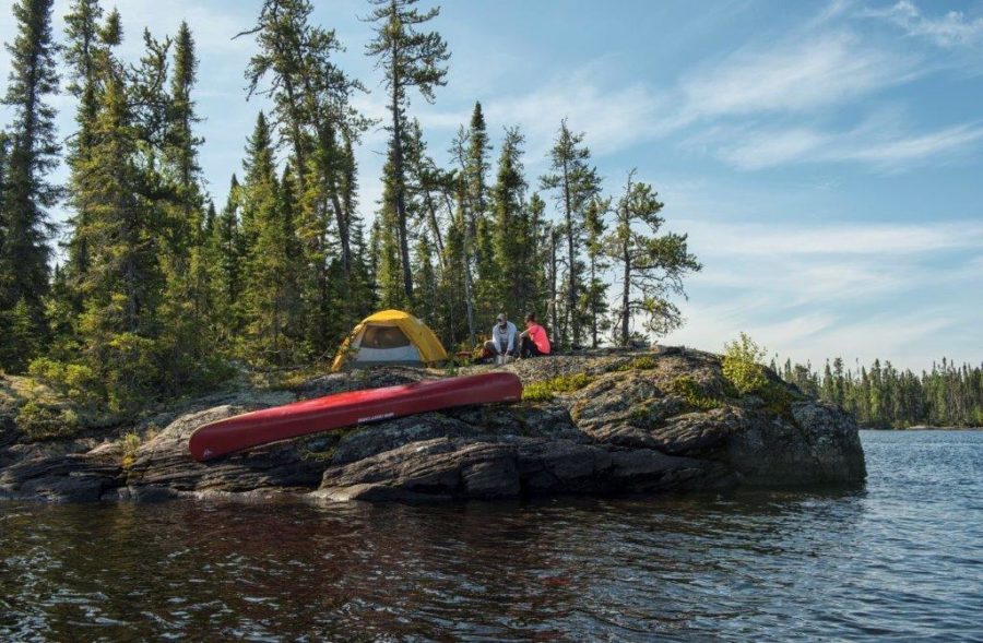 A rocky outcrop into a lake, with a canoe and tent sent up in the foreground of boreal forest
