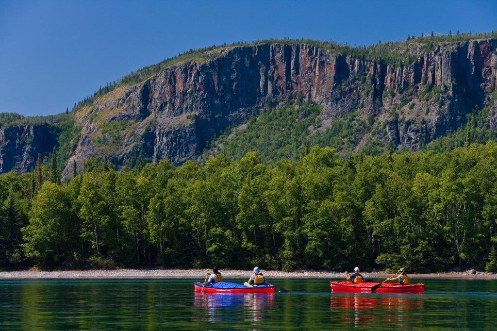 Two red canoes glide by tall cliffs on clear greenish water