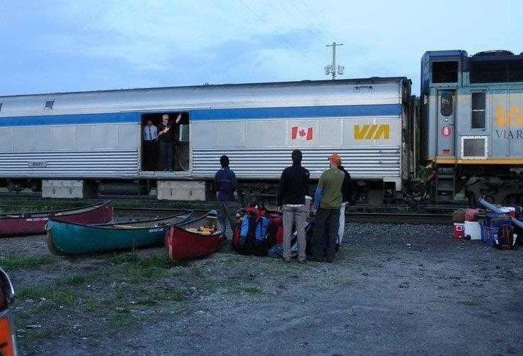 Side of a train at dusk with people unloading canoes