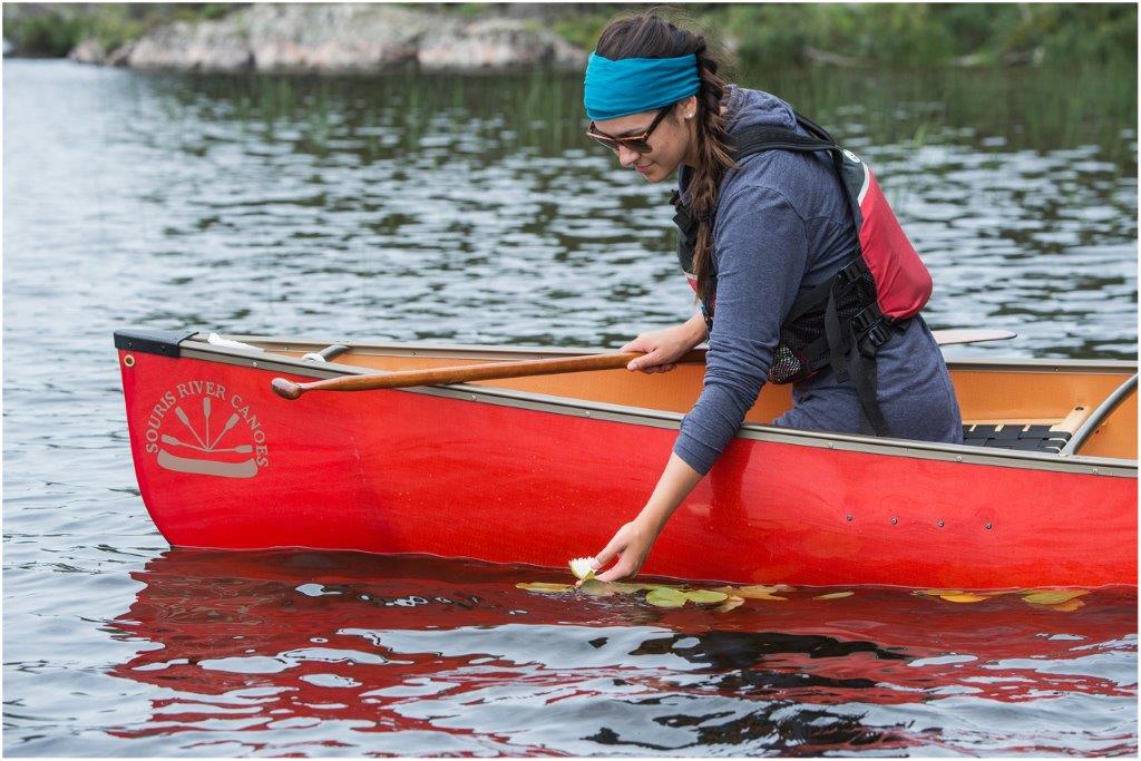 Une jeune femme dans un canot rouge, la main dans l’eau.