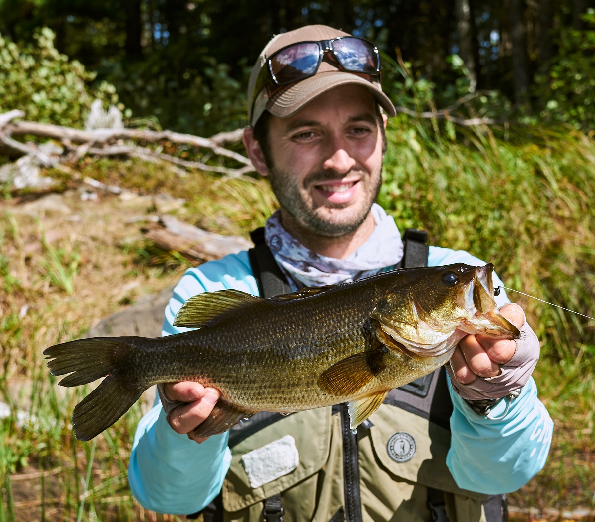 Man with brown cap holding up a largemouth bass