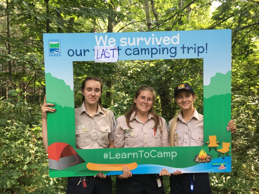 Trois personnes posant à l’intérieur d’un cadre qui dit « Nous avons survécu à notre dernière excursion de camping »
