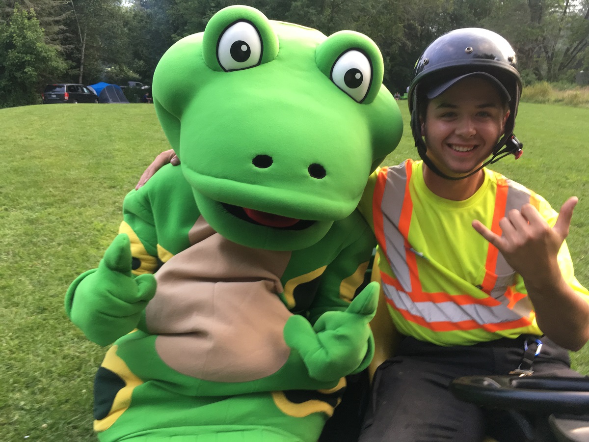 Une grenouille-mascotte photographiée avec un enfant portant un casque