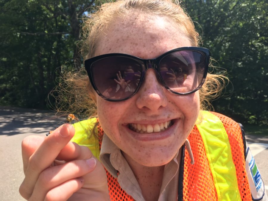 Girl with sunglasses and dragonfly on her finger, smiling at the camera