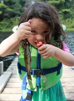 Petite fille tenant un poisson attrapé à l’aide d’un flotteur rose