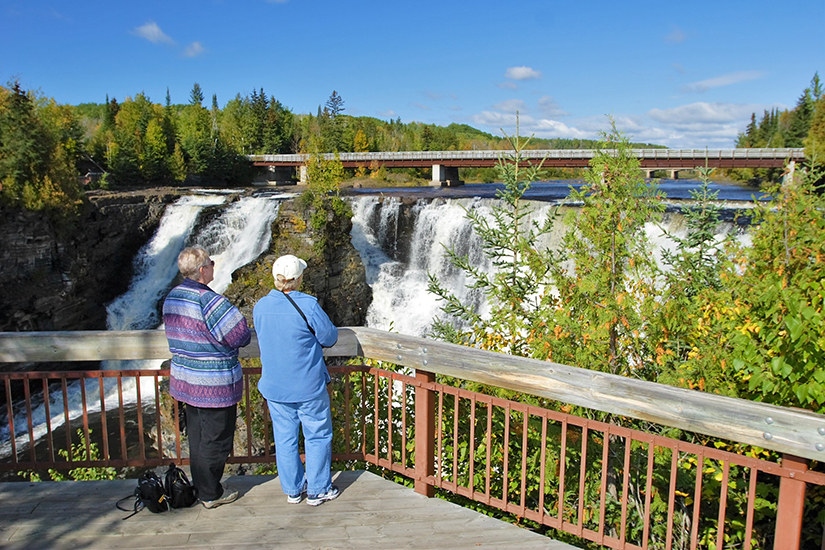 Two women stand on platform watching waterfall. 