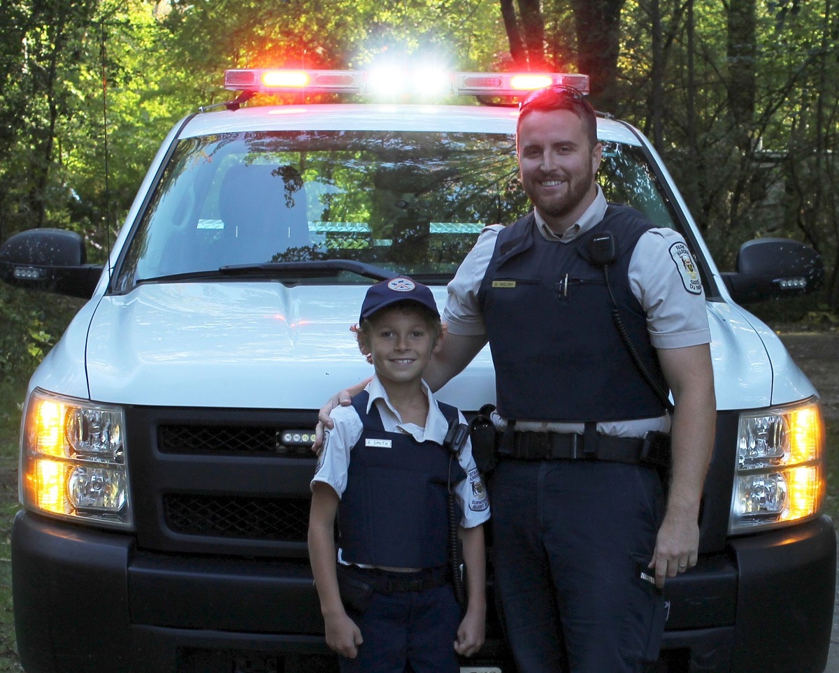 Park warden with child in in front of park vehicle with lights on the vehicle