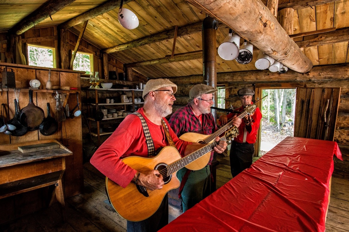 Trois hommes jouent des instruments de musique dans une cabane