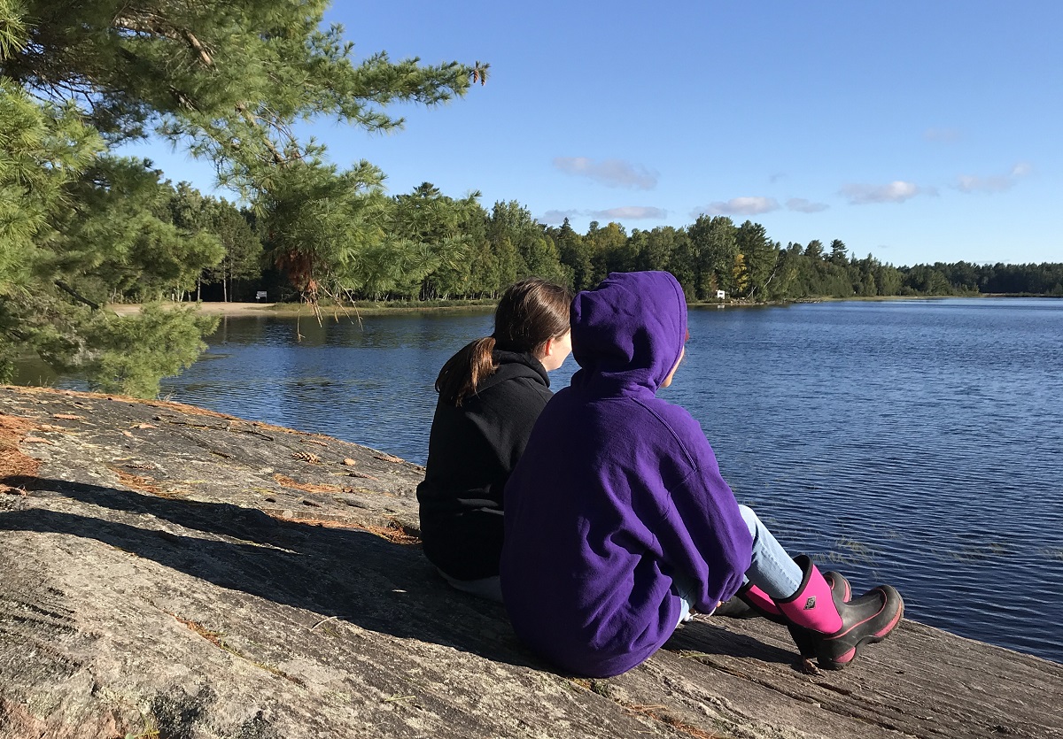 Les deux jeunes filles sur la berge, observant le lac. 