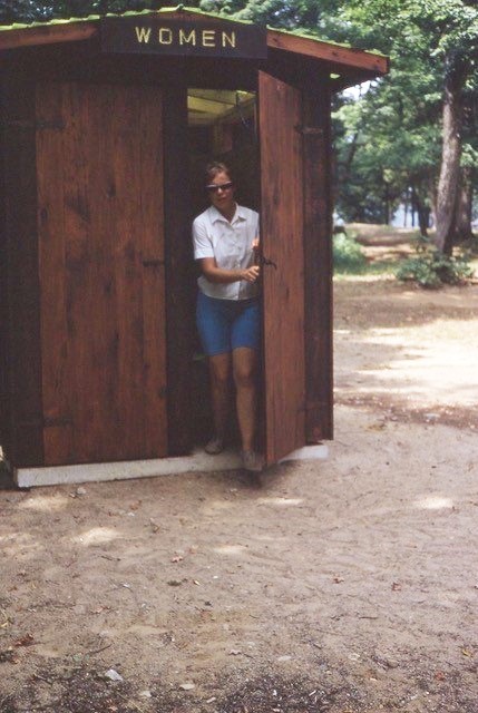 Woman emerging from a single stall outhouse 