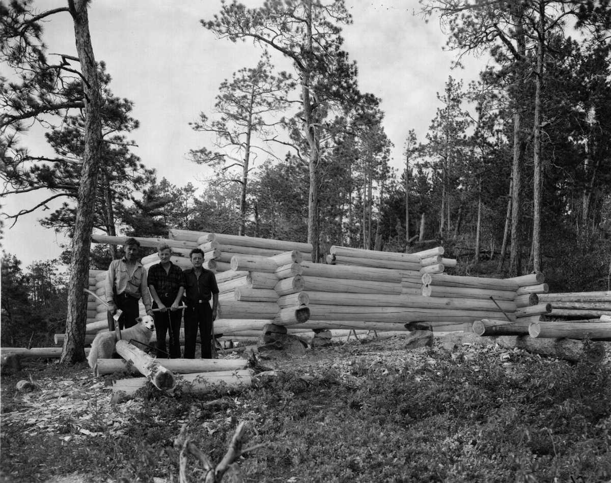Three men in front of the beginning of a log ranger cabin