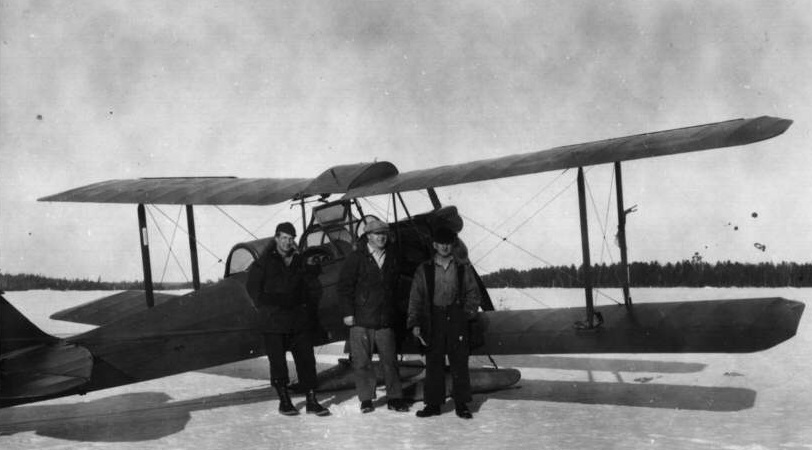 Photo en noir et blanc de trois types devant un avion de brousse