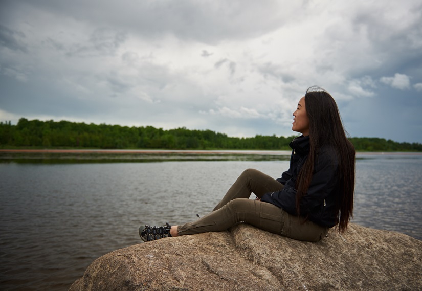 Woman sits on rock by lake