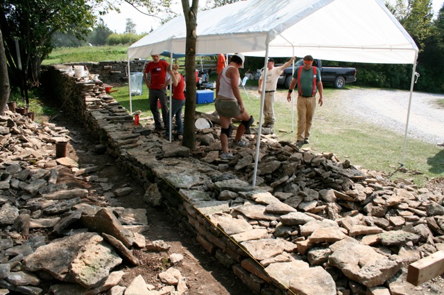 stone wall with volunteers standing under sun shelter