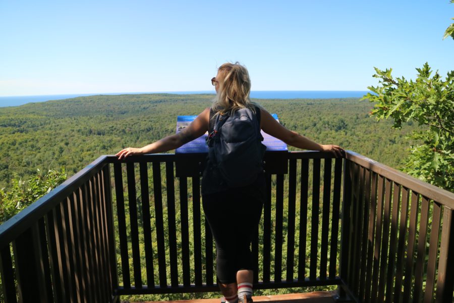 Une femme observant les arbres et l’eau au loin depuis un observatoire en bois.