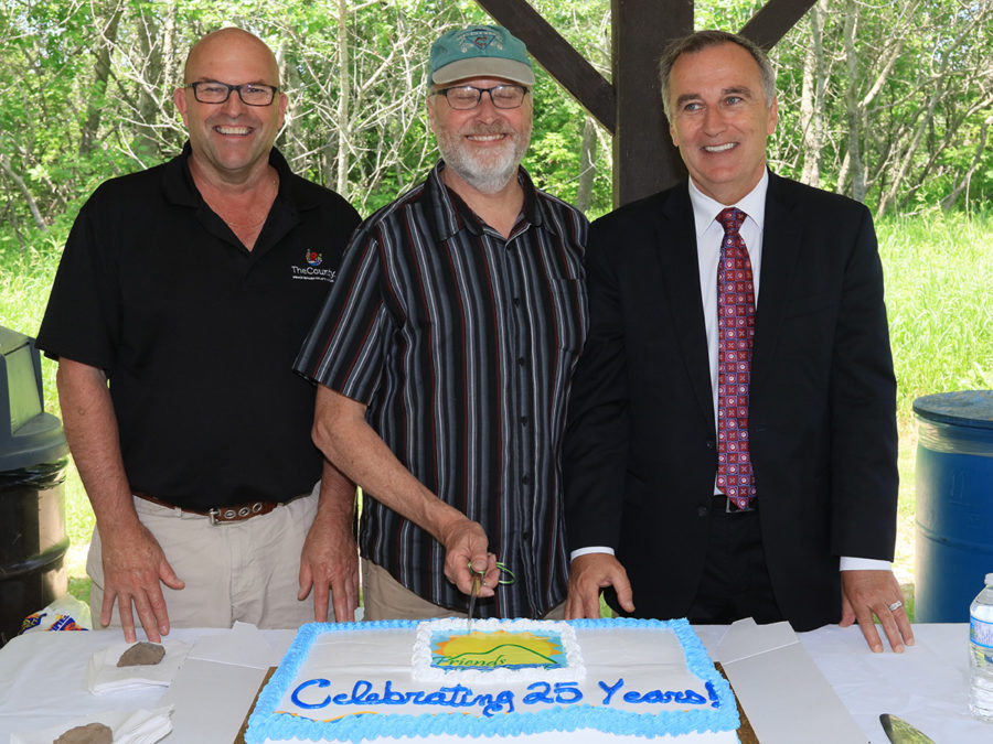 three men cutting cake that says "celebrating 25 years!"
