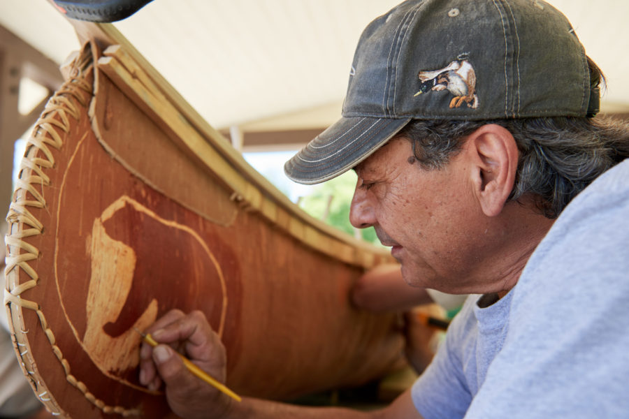 Indigenous person etching a bear into the side of a birch bark canoe