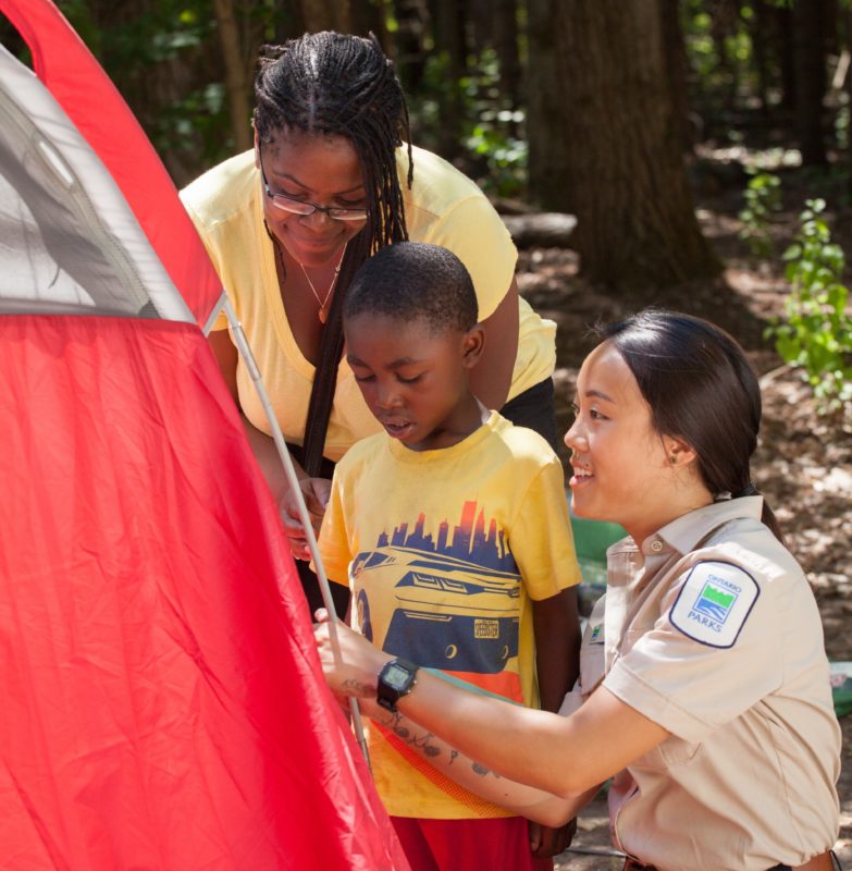 Ontario Parks Staff showing a mother and son how to set up a tent.