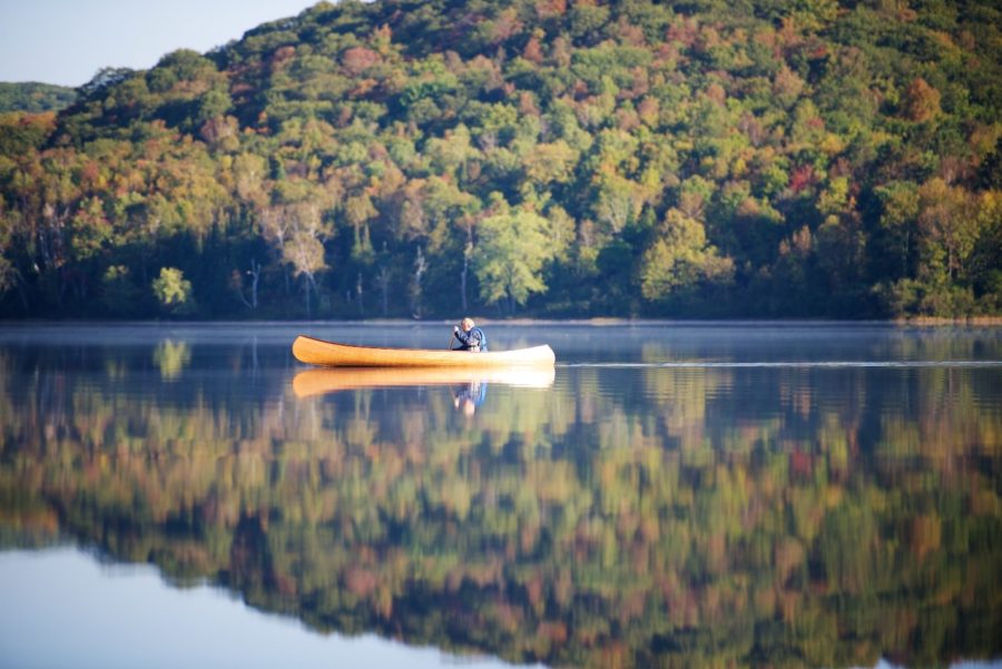 man in canoe on water, reflecting trees
