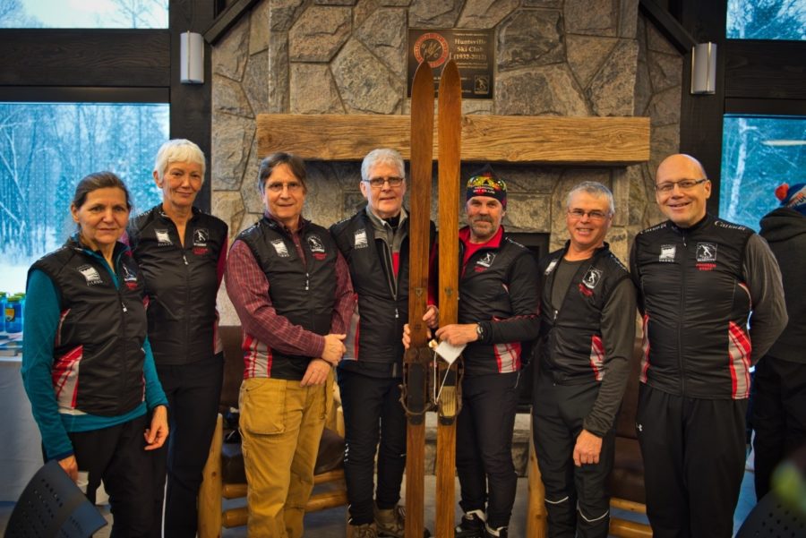 Ski club standing in front of fireplace holding classic skis