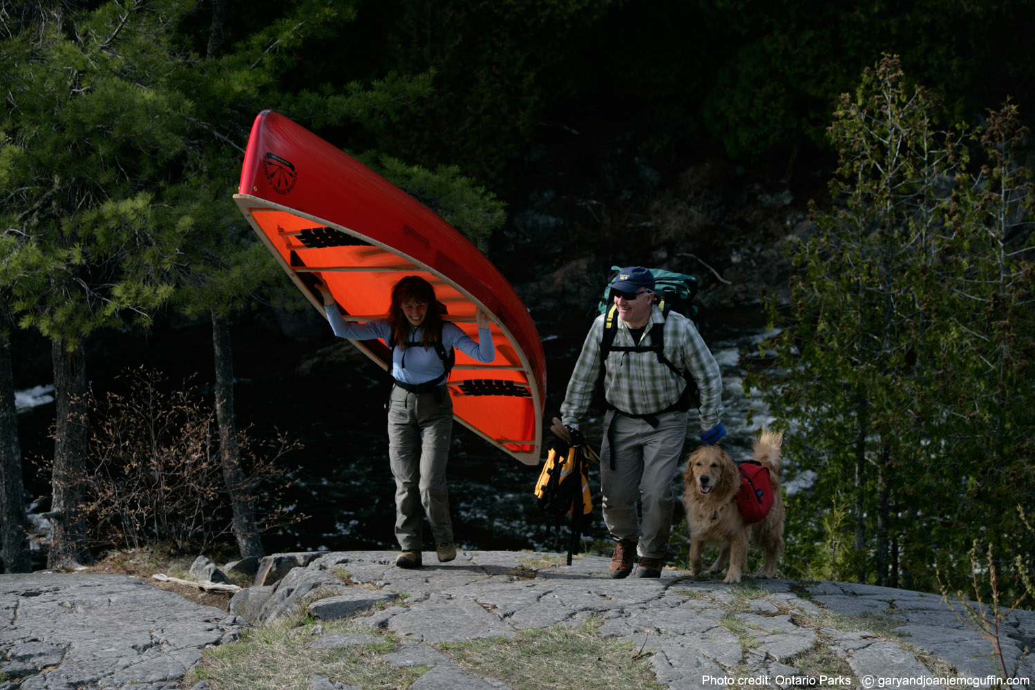 woman portaging canoe with man and dog