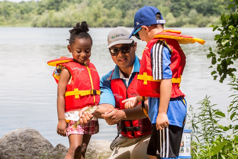 Instructeur montrant un poisson à deux enfants au bord d’un lac