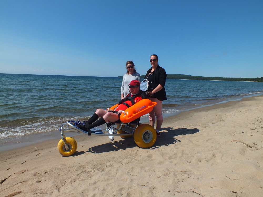 People on the shore at Pancake Bay, one person in a Mobi wheelchair.