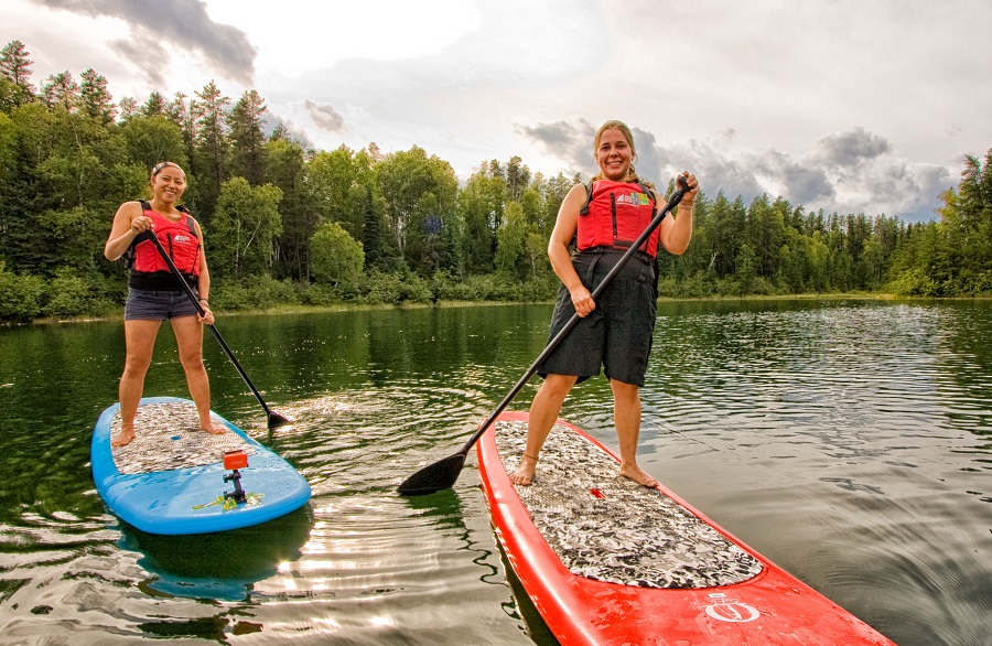 Two women on standup paddleboards wearing life jackets.