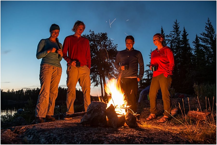 Four people standing by a fire holding mugs and smiling