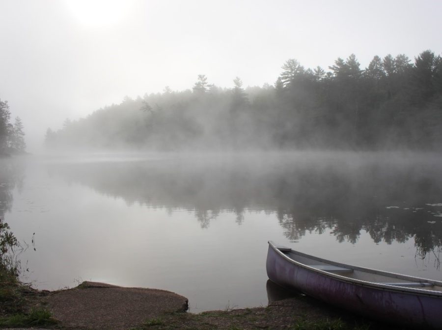 A canoe sitting by a misty lake on a summer morning