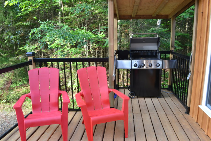 On the porch you see four red muskoka chairs and a covered barbeque area.