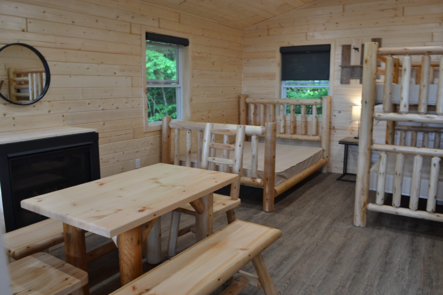 View of inside the cabin showing dinning table, queen size bed, and the double bunks.