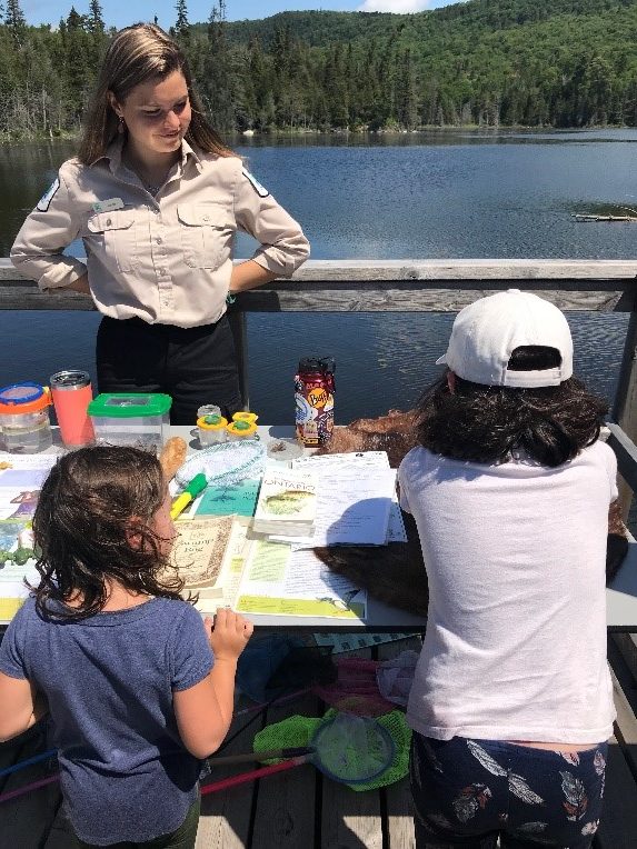 Jordan at Trapper’s Trail for a Children’s Wetland Program. Seen are two children exploring the display table with the water in the background.