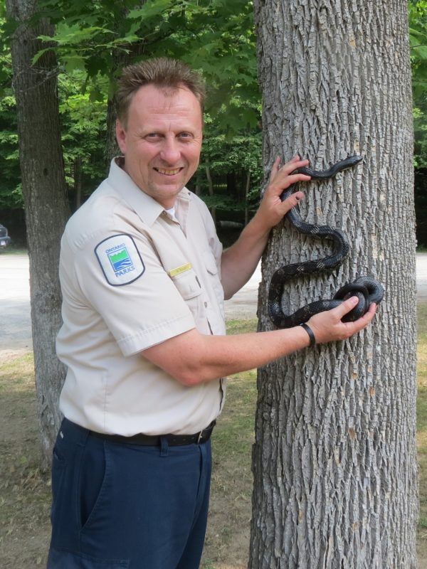 Mark holding rat snake besides tree