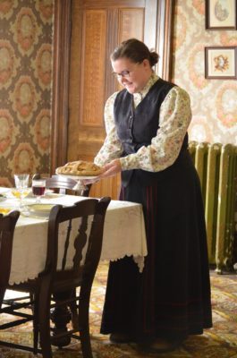 Une membre du personnel servant le repas dans une tenue qui respecte les règles vestimentaires de l’époque