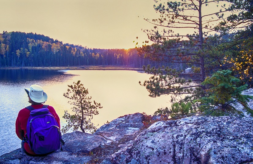 Randonneuse assise sur un rocher, regardant le lac.