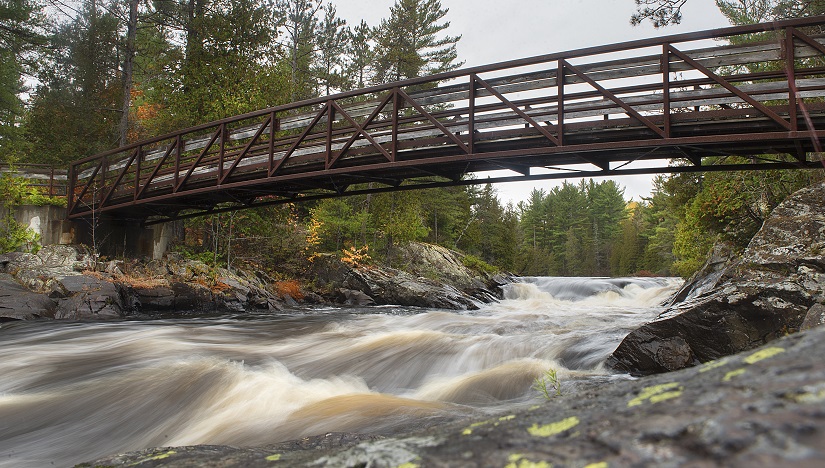 rivière dévalant sous un pont entouré des couleurs d’automne