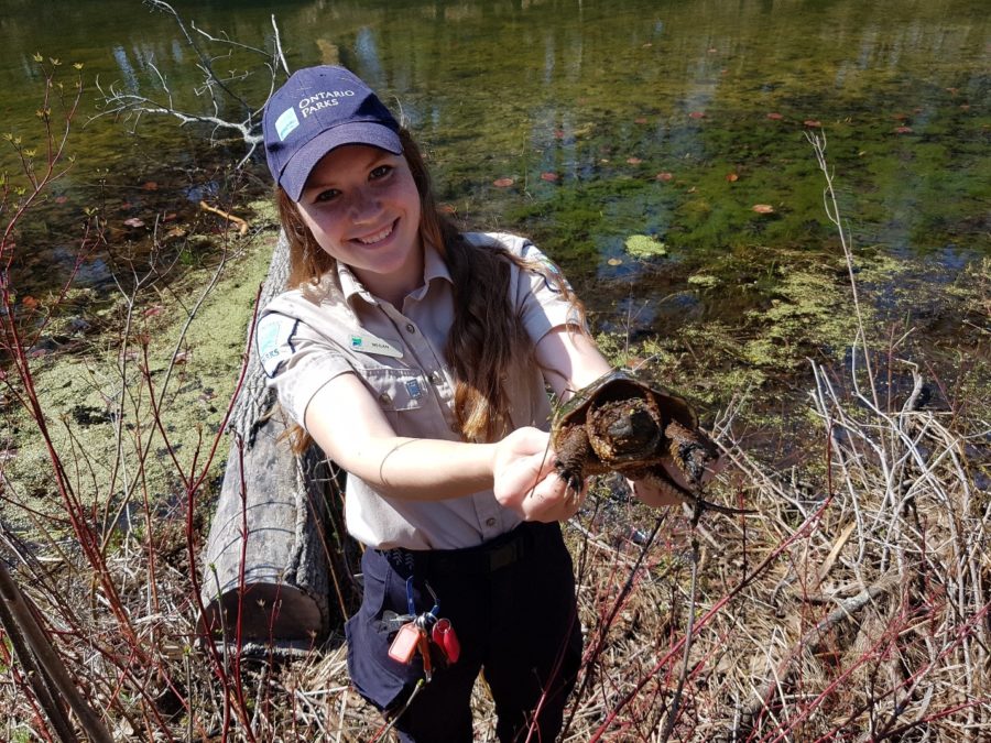 Staff member by the river holding up a snapping turtle.