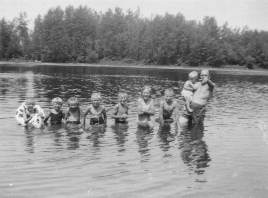 Family photo showing 8 siblings and father standing in the river.