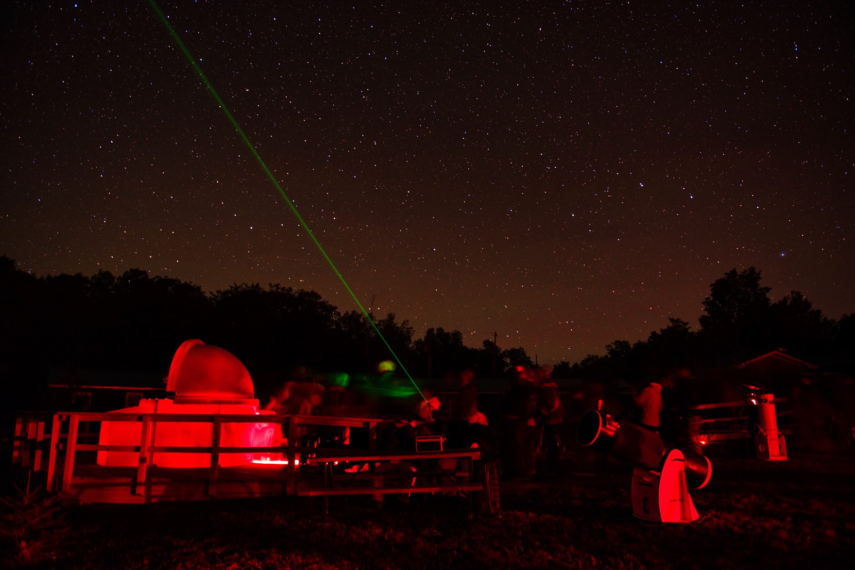 Des personnes profitant du complexe de l'observatoire de Killarney la nuit. Observatoire avec laser pointant vers les constellations.