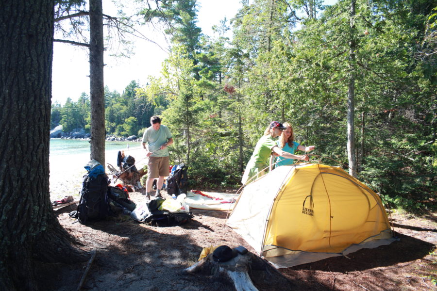 Deux personnes près d’une tente et une autre au bord d’un lac