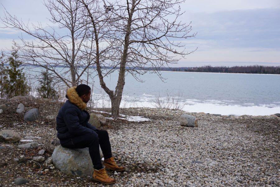 Un randonneur assis sur un rocher à côté du rivage enneigé
