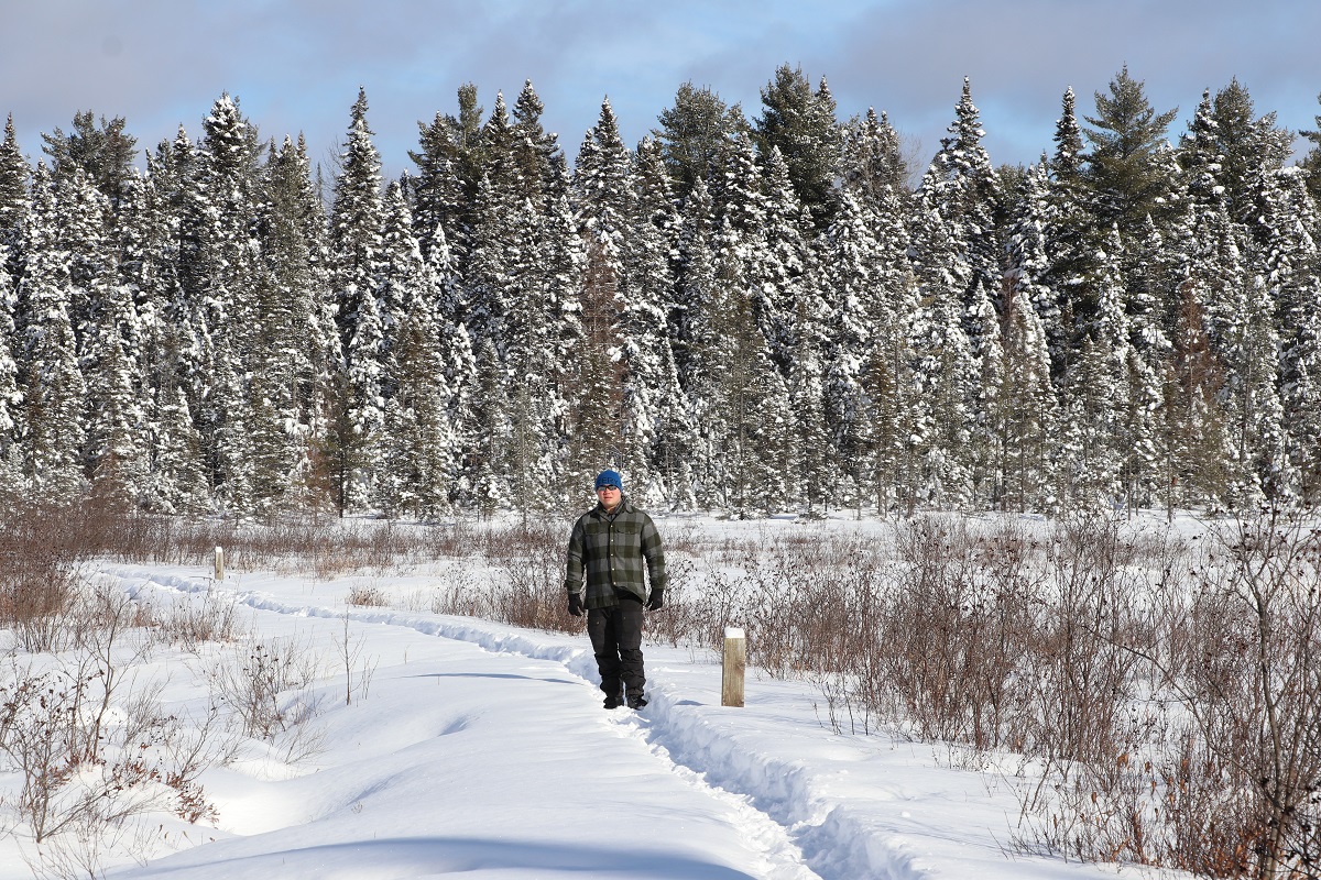 Solitary man walks on a trail in the winter with trees behind him.